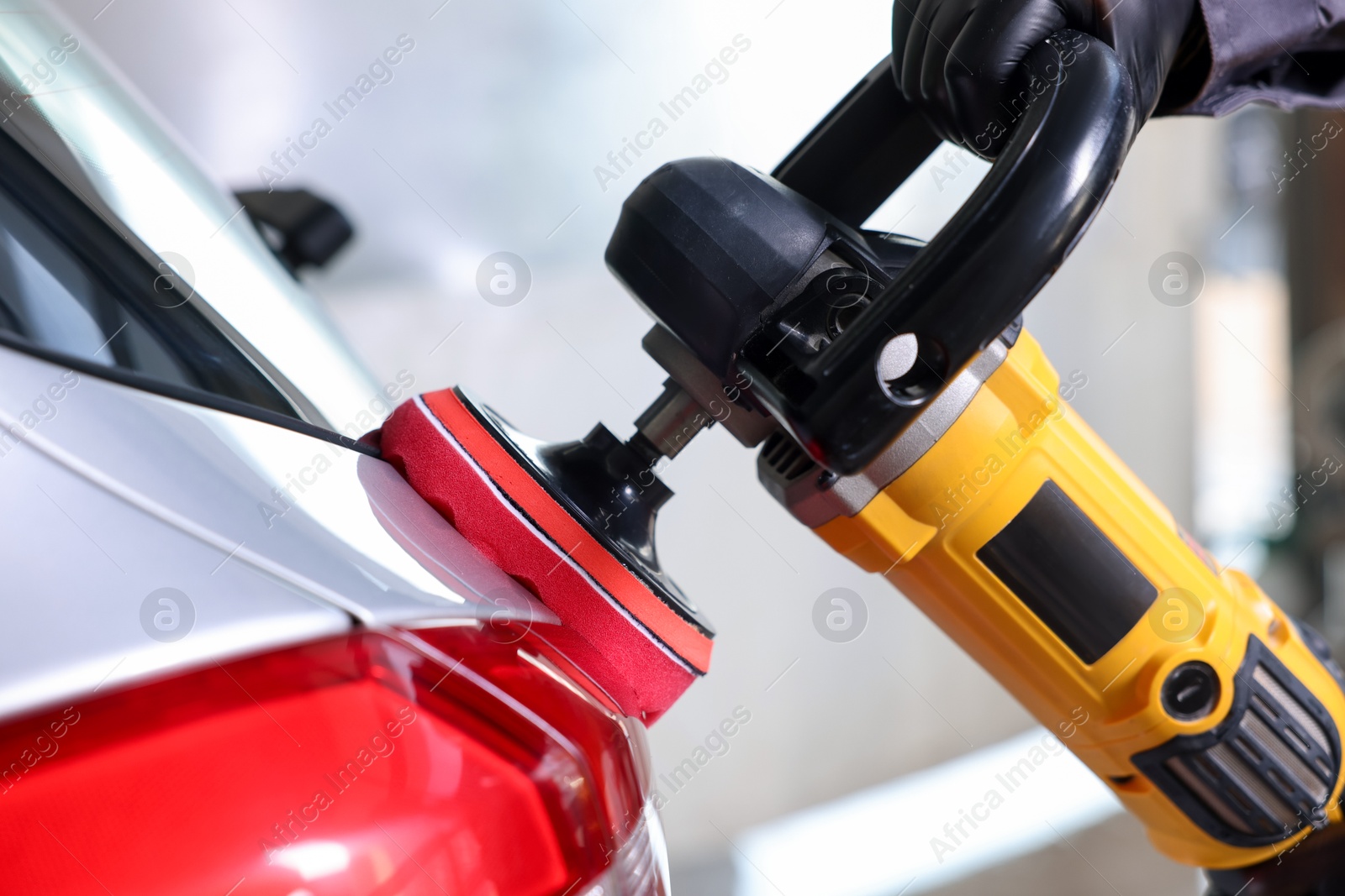 Photo of Man polishing car with orbital polisher indoors, closeup