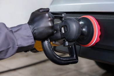 Photo of Man polishing car with orbital polisher indoors, closeup