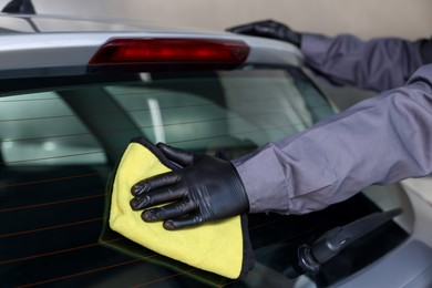 Photo of Man polishing car rear window with yellow rag indoors, closeup