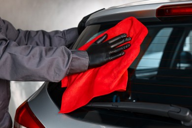 Photo of Man polishing car rear window with red rag indoors, closeup