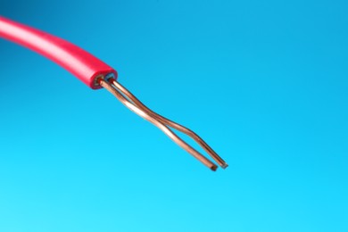 Photo of Stripped electrical wire with copper strands on light blue background, closeup