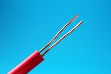 Photo of Stripped electrical wire with copper strands on light blue background, closeup