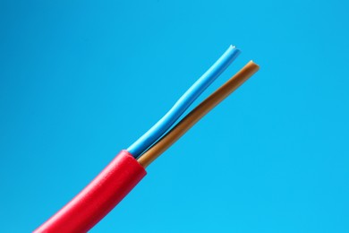 Photo of Red stripped electrical wire on light blue background, closeup