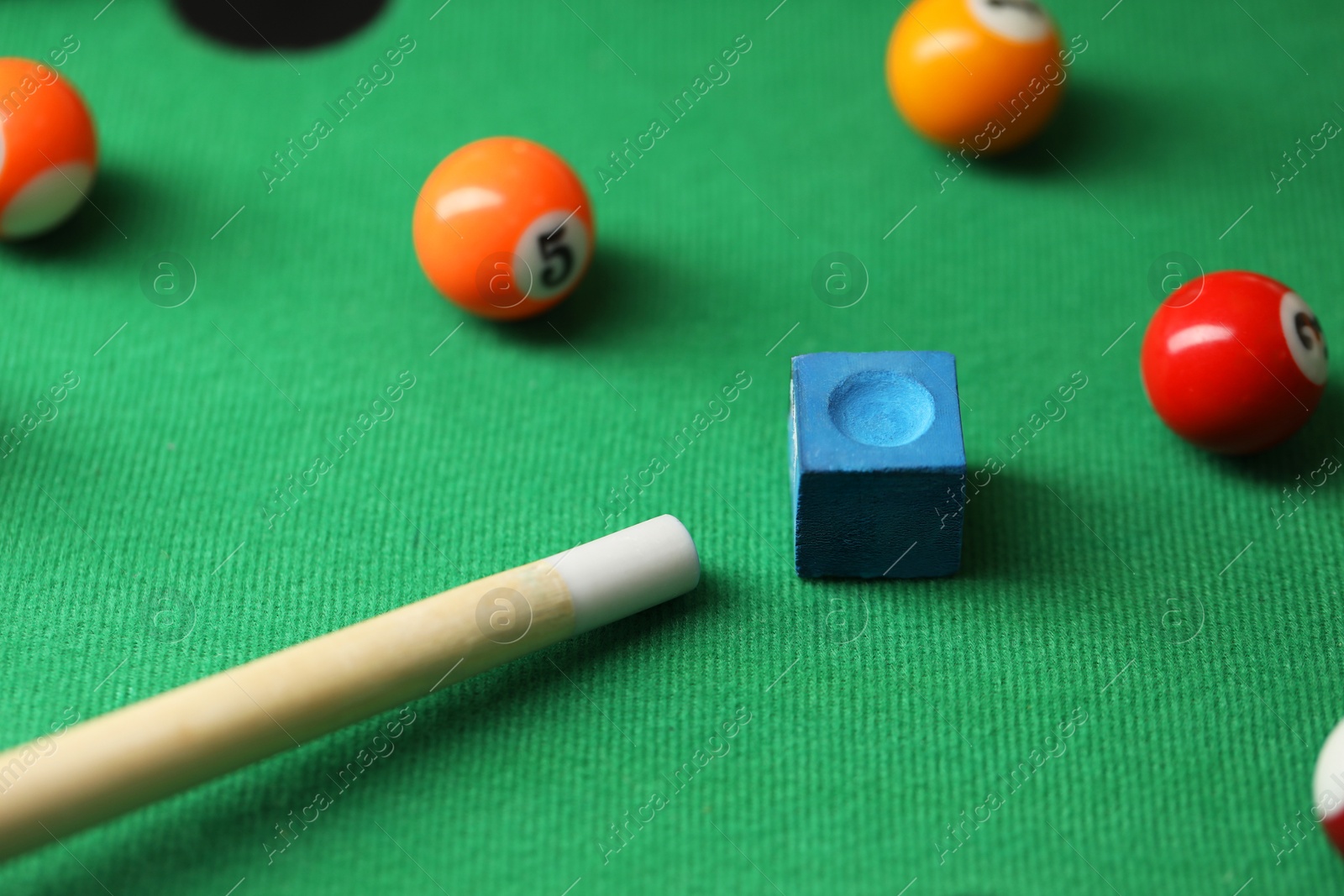 Photo of Colorful billiard balls, cue and chalk on green table, closeup