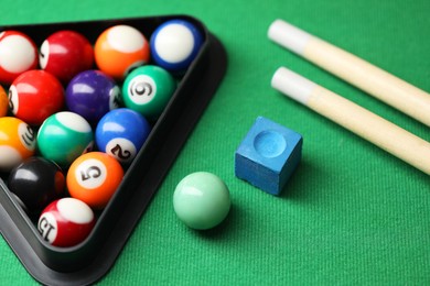 Photo of Many colorful billiard balls in triangle rack, cues and chalk on green table, closeup