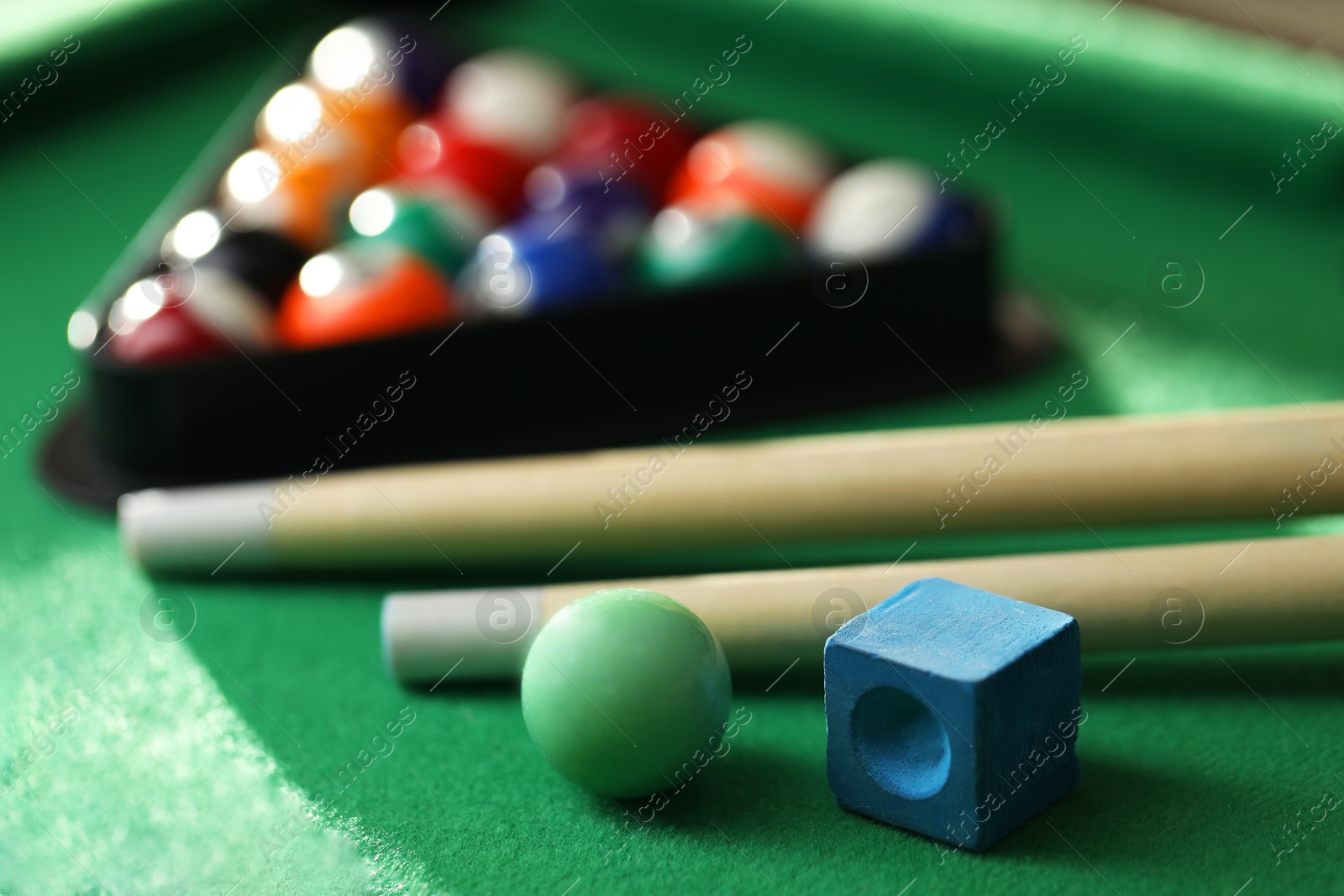 Photo of Many colorful billiard balls in triangle rack, cues and chalk on green table, closeup