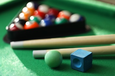 Photo of Many colorful billiard balls in triangle rack, cues and chalk on green table, closeup