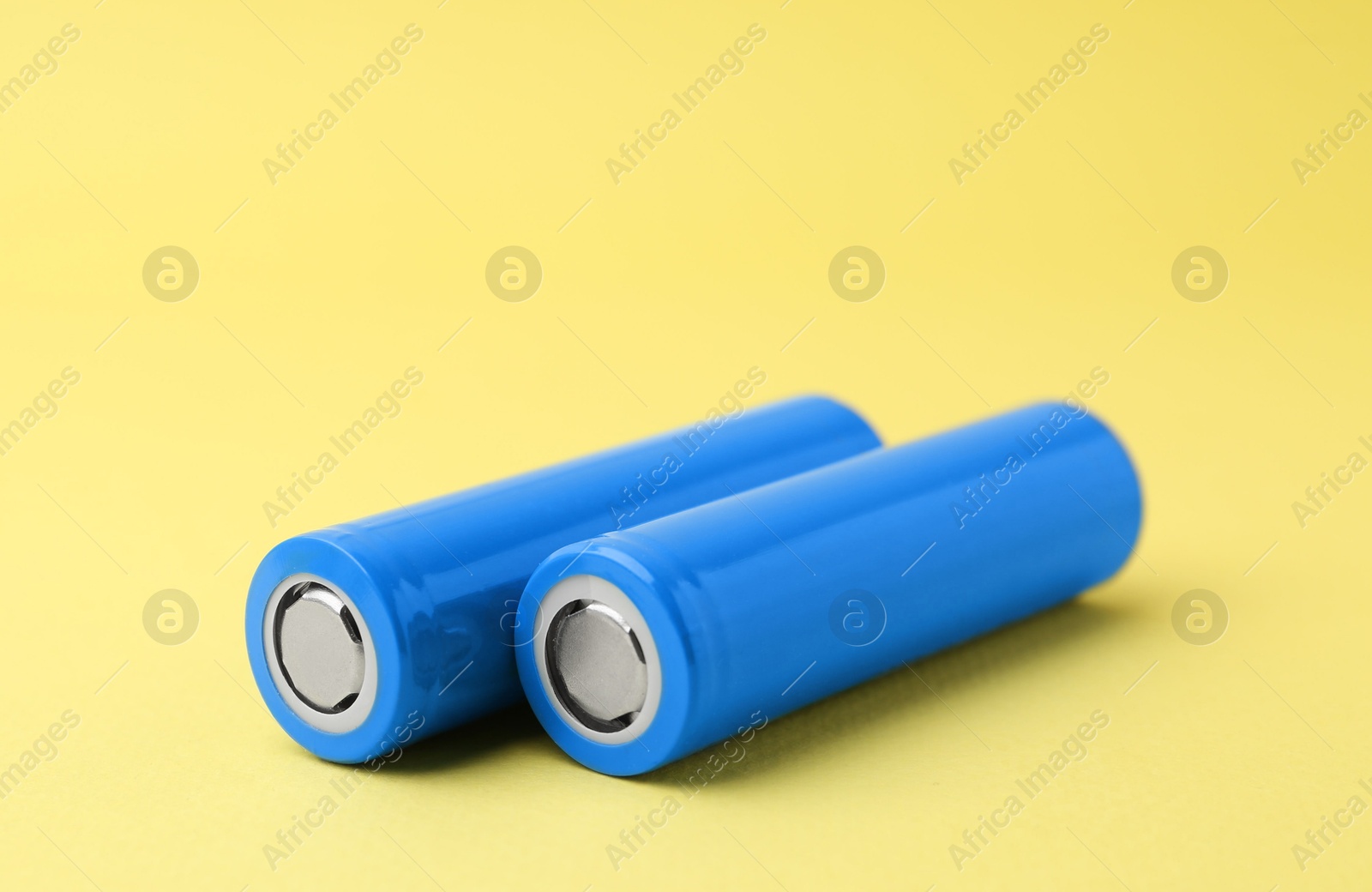 Photo of Two AA cell batteries on yellow background, closeup. Space for text