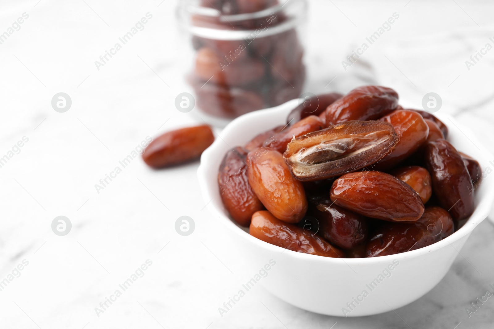 Photo of Tasty dried dates in bowl and jar on white marble table, closeup. Space for text