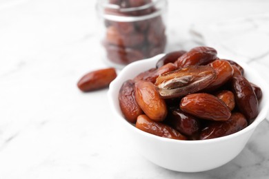 Photo of Tasty dried dates in bowl and jar on white marble table, closeup. Space for text