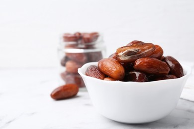 Photo of Tasty dried dates in bowl and jar on white marble table, closeup. Space for text