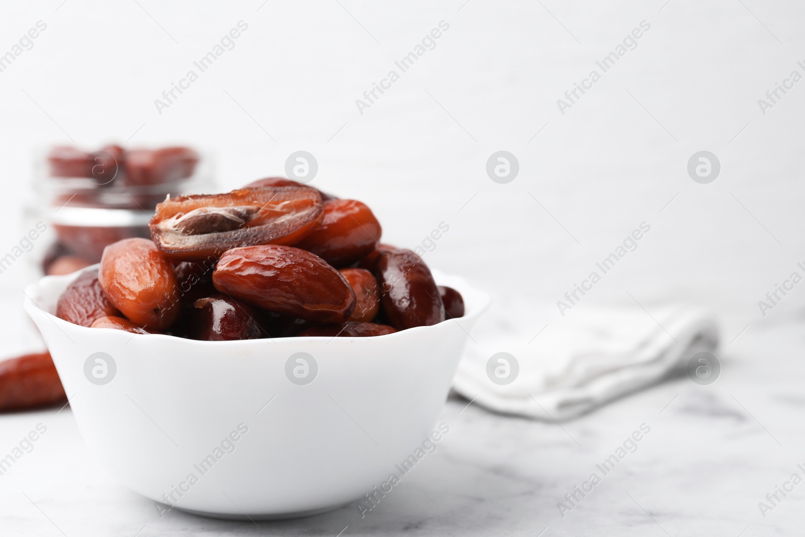 Photo of Tasty dried dates in bowl and jar on white marble table, closeup. Space for text