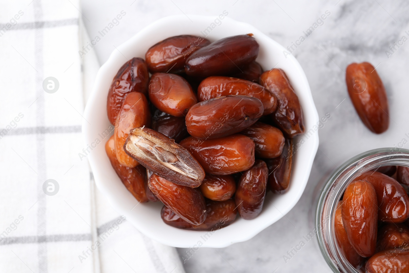 Photo of Tasty sweet dried dates in bowl and jar on white marble table, flat lay