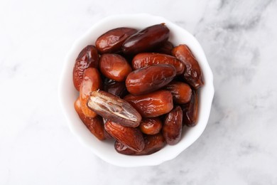 Photo of Tasty dried dates in bowl on white marble table, top view