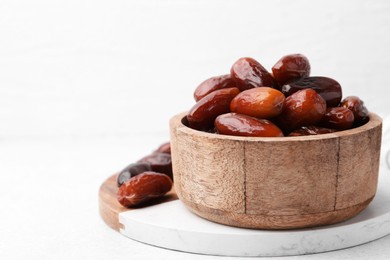 Photo of Tasty dried dates in wooden bowl on white table, closeup. Space for text