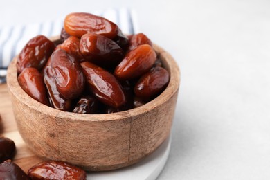 Photo of Tasty dried dates in wooden bowl on white table, closeup. Space for text