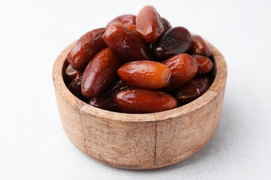 Photo of Tasty dried dates in wooden bowl on white table, closeup