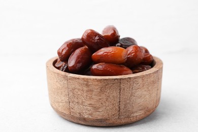 Photo of Tasty dried dates in wooden bowl on white table, closeup