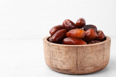 Photo of Tasty dried dates in wooden bowl on white table, closeup