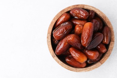 Photo of Tasty dried dates in wooden bowl on white table, top view. Space for text