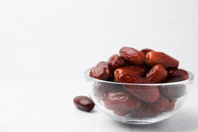 Photo of Tasty dried dates in glass bowl on white table, closeup. Space for text