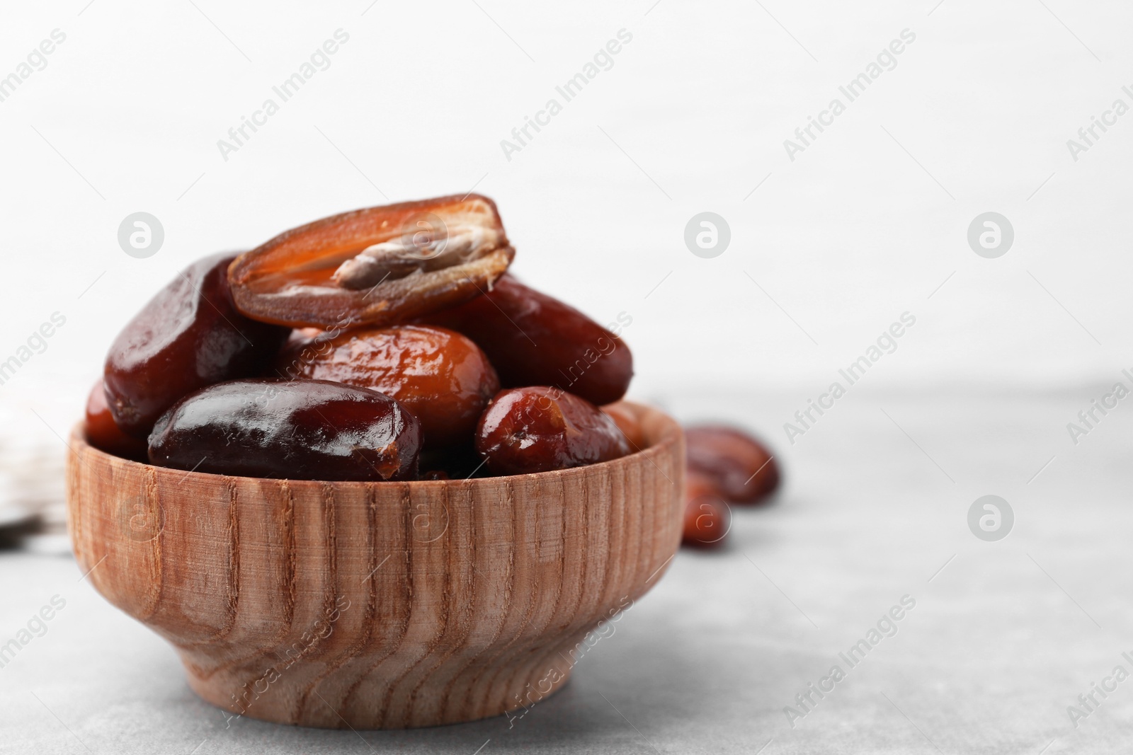 Photo of Tasty dried dates in bowl on light grey table, closeup. Space for text