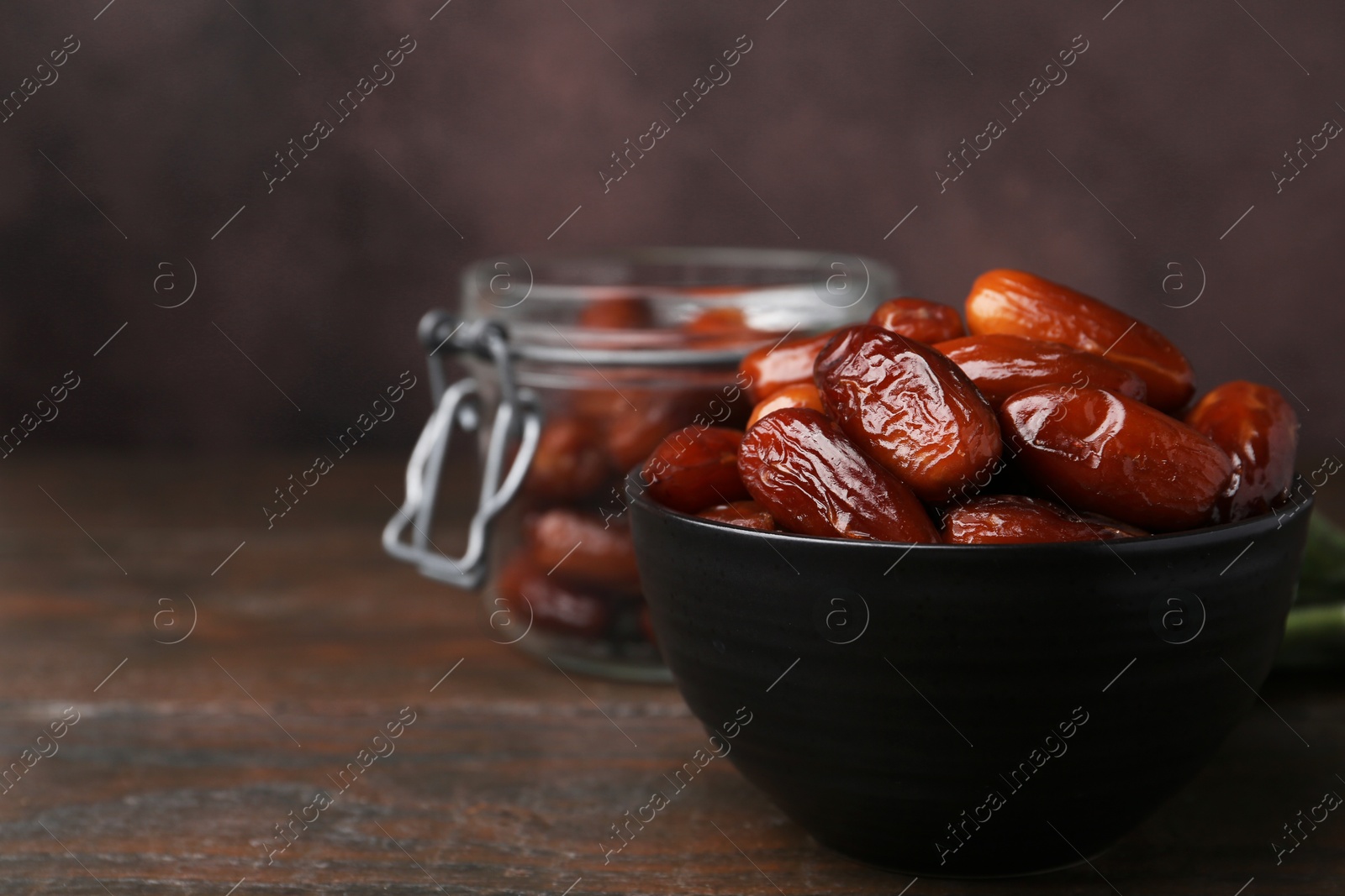 Photo of Tasty dried dates in bowl and jar on wooden table, closeup. Space for text