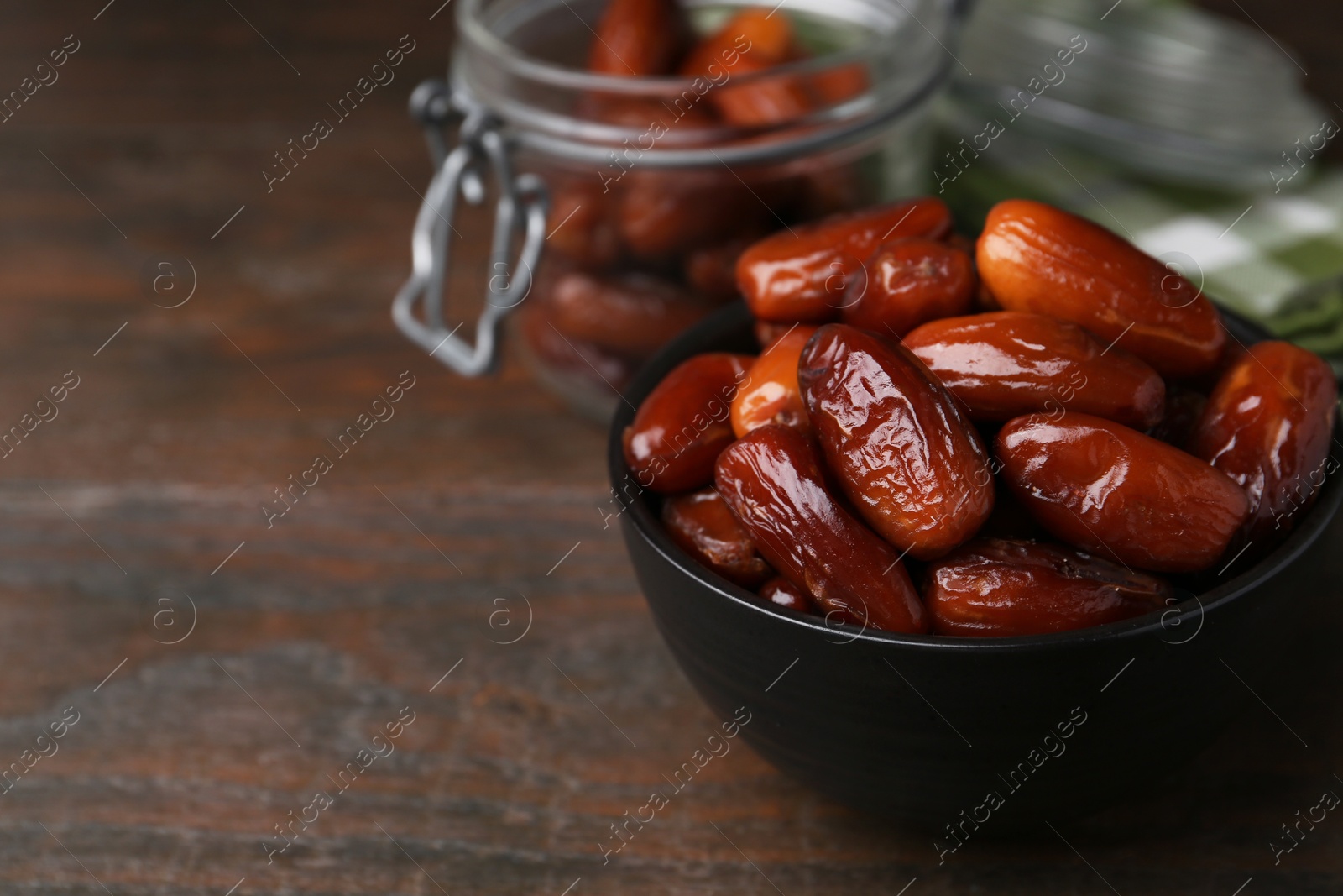 Photo of Tasty dried dates in bowl and jar on wooden table, closeup. Space for text