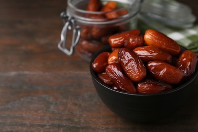 Photo of Tasty dried dates in bowl and jar on wooden table, closeup. Space for text