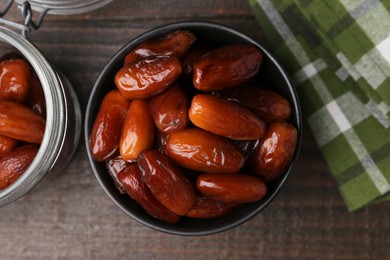 Photo of Tasty dried dates in bowl and jar on wooden table, flat lay