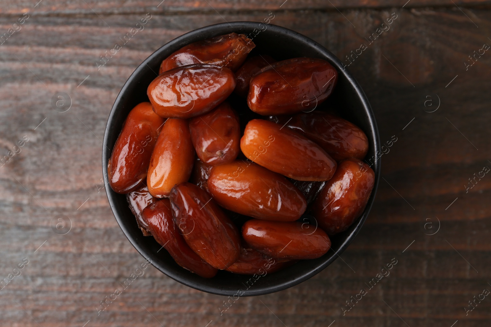 Photo of Tasty dried dates in bowl on wooden table, top view