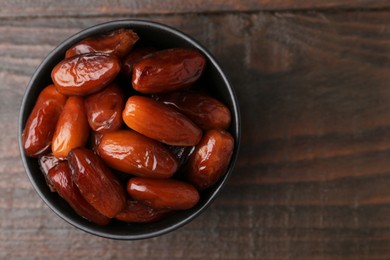 Photo of Tasty dried dates in bowl on wooden table, top view. Space for text