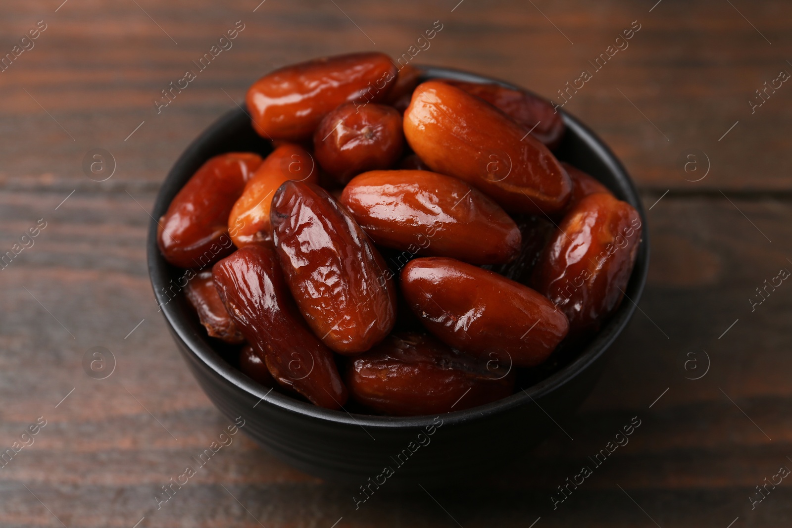 Photo of Tasty dried dates in bowl on wooden table, closeup