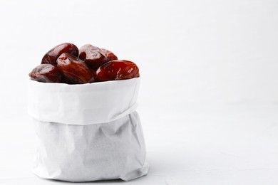 Photo of Tasty sweet dried dates in paper bag on white table, closeup. Space for text