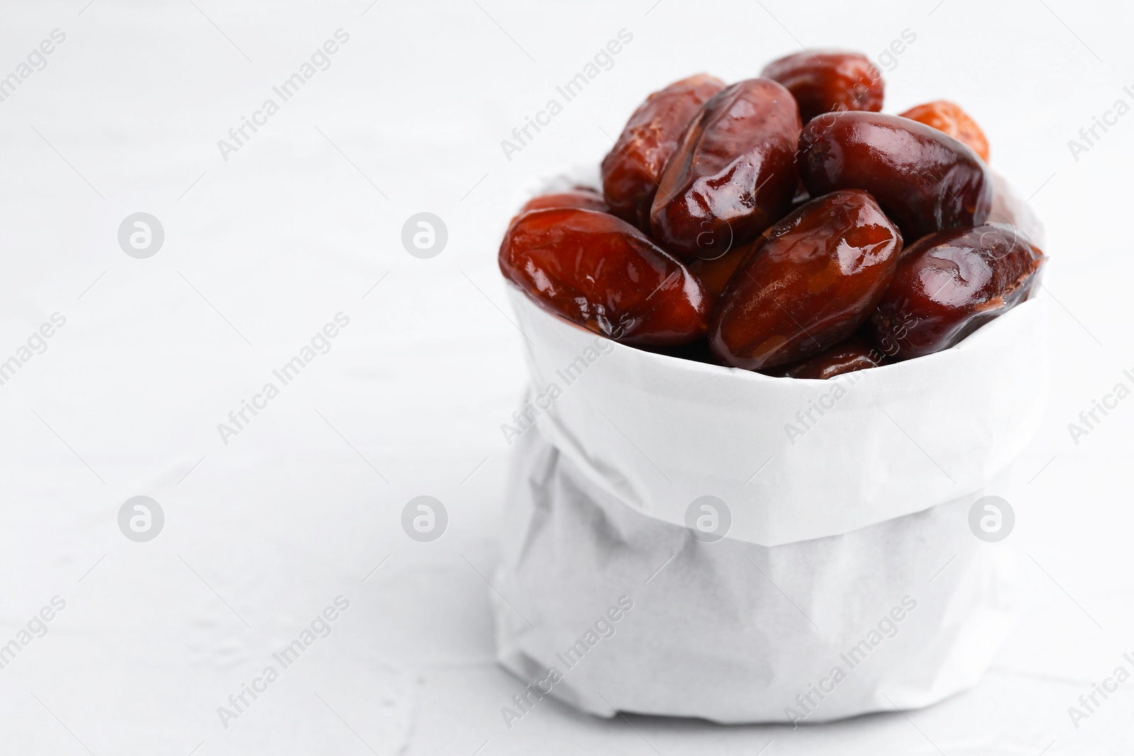 Photo of Tasty sweet dried dates in paper bag on white table, closeup. Space for text