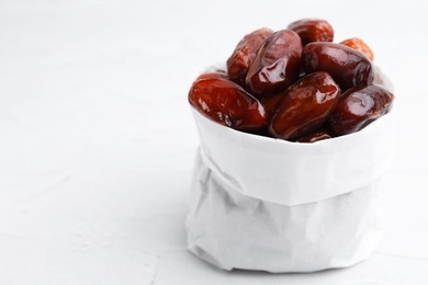 Photo of Tasty sweet dried dates in paper bag on white table, closeup. Space for text