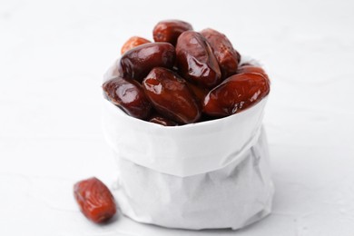 Photo of Tasty sweet dried dates in paper bag on white table, closeup