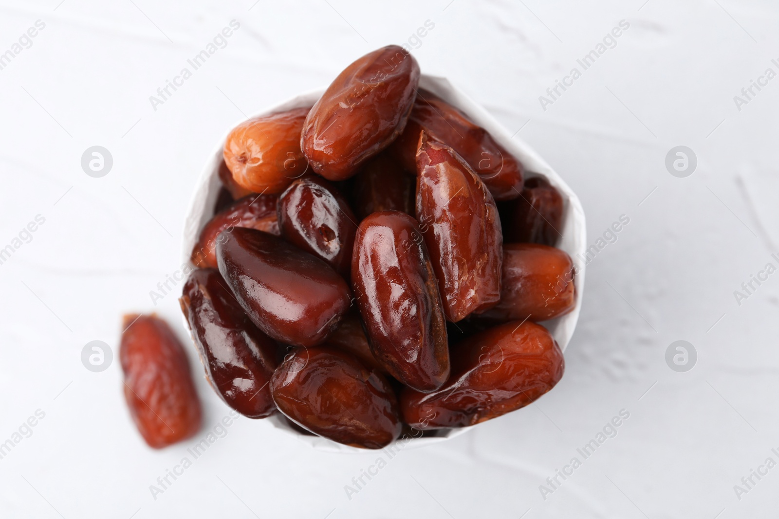 Photo of Tasty sweet dried dates in paper bag on white table, top view