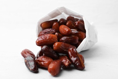 Photo of Tasty sweet dried dates in paper bag on white table, closeup