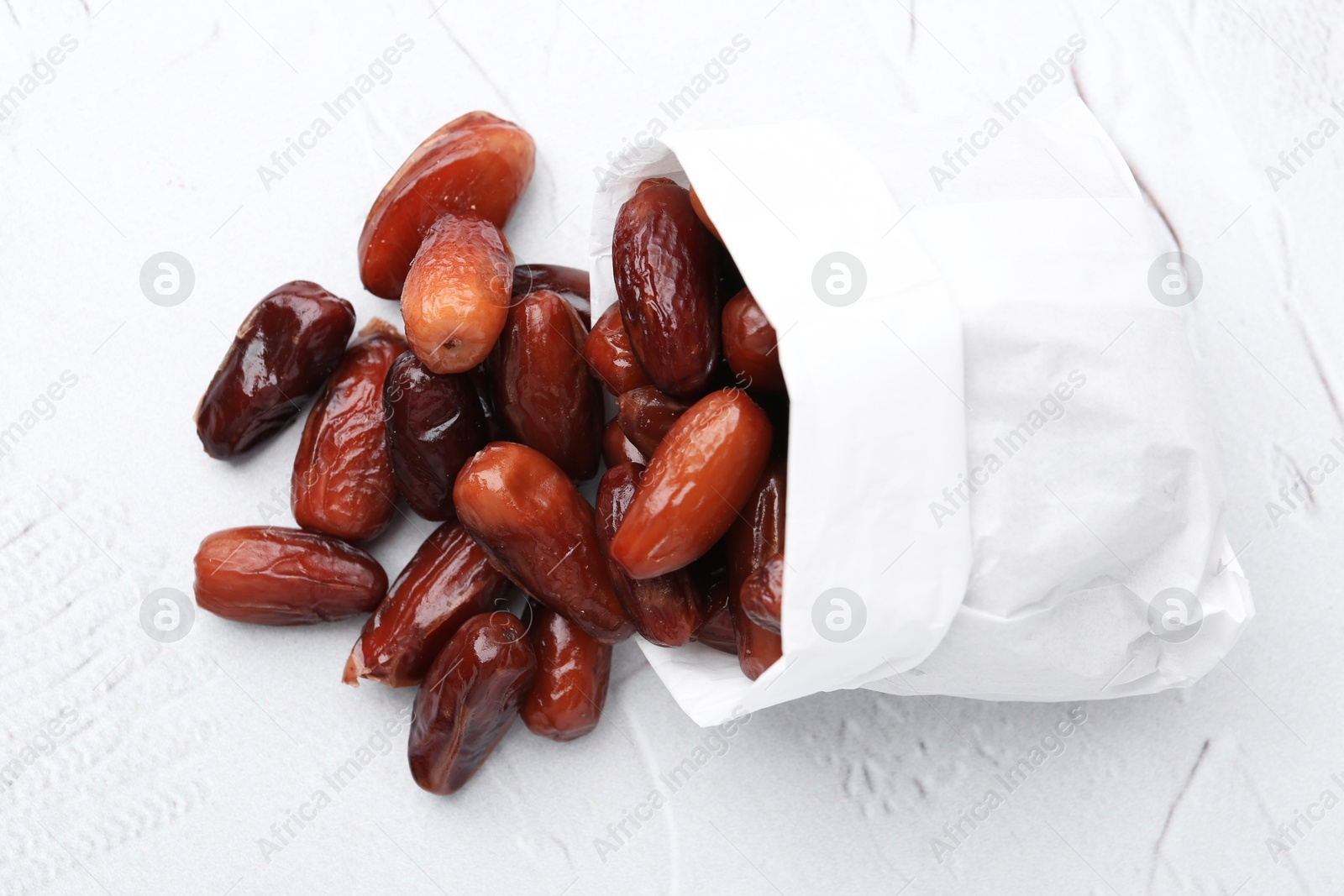 Photo of Tasty sweet dried dates in paper bag on white table, top view