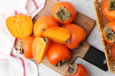 Photo of Whole and cut ripe persimmons on white table, flat lay