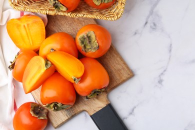 Whole and cut ripe persimmons on white marble table, flat lay. Space for text