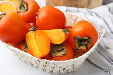 Ripe persimmons in wicker basket on white tiled table, closeup