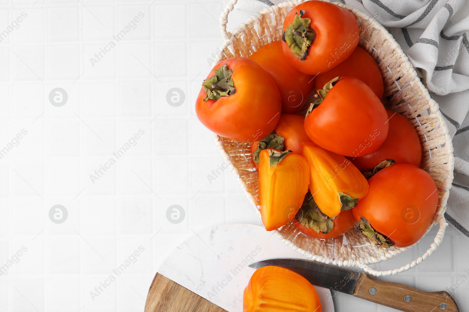 Photo of Ripe persimmons in wicker basket on white tiled table, top view. Space for text