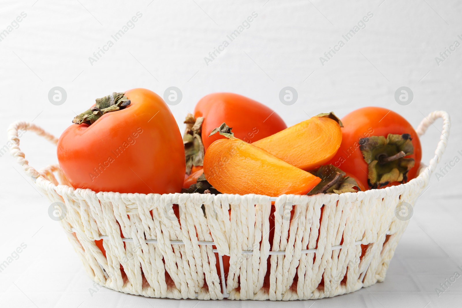 Photo of Ripe persimmons in wicker basket on white tiled table