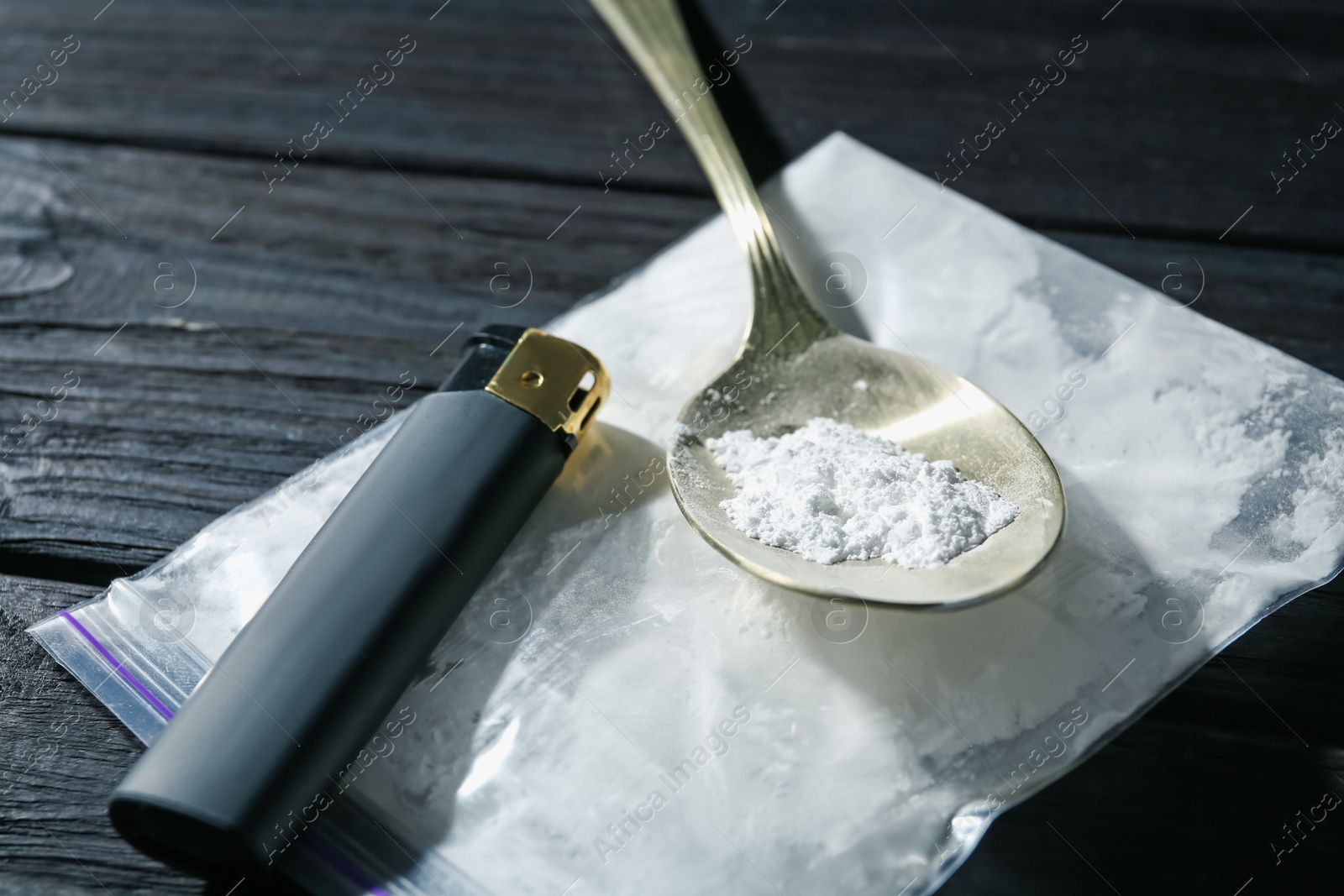 Photo of Drug addiction. Plastic bag with powder, spoon and cigarette lighter on black wooden table, closeup