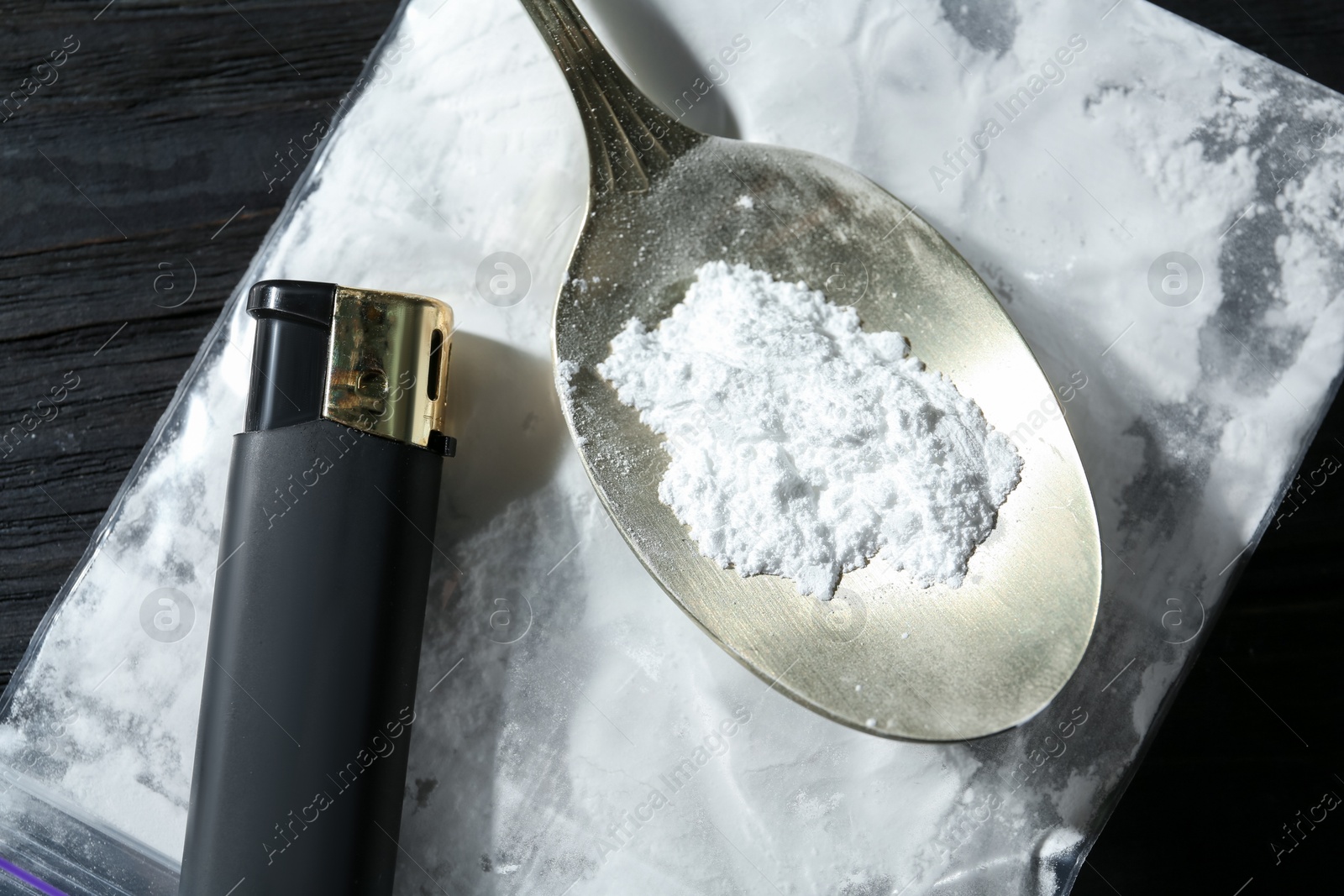 Photo of Drug addiction. Plastic bag with powder, spoon and cigarette lighter on black wooden table, top view