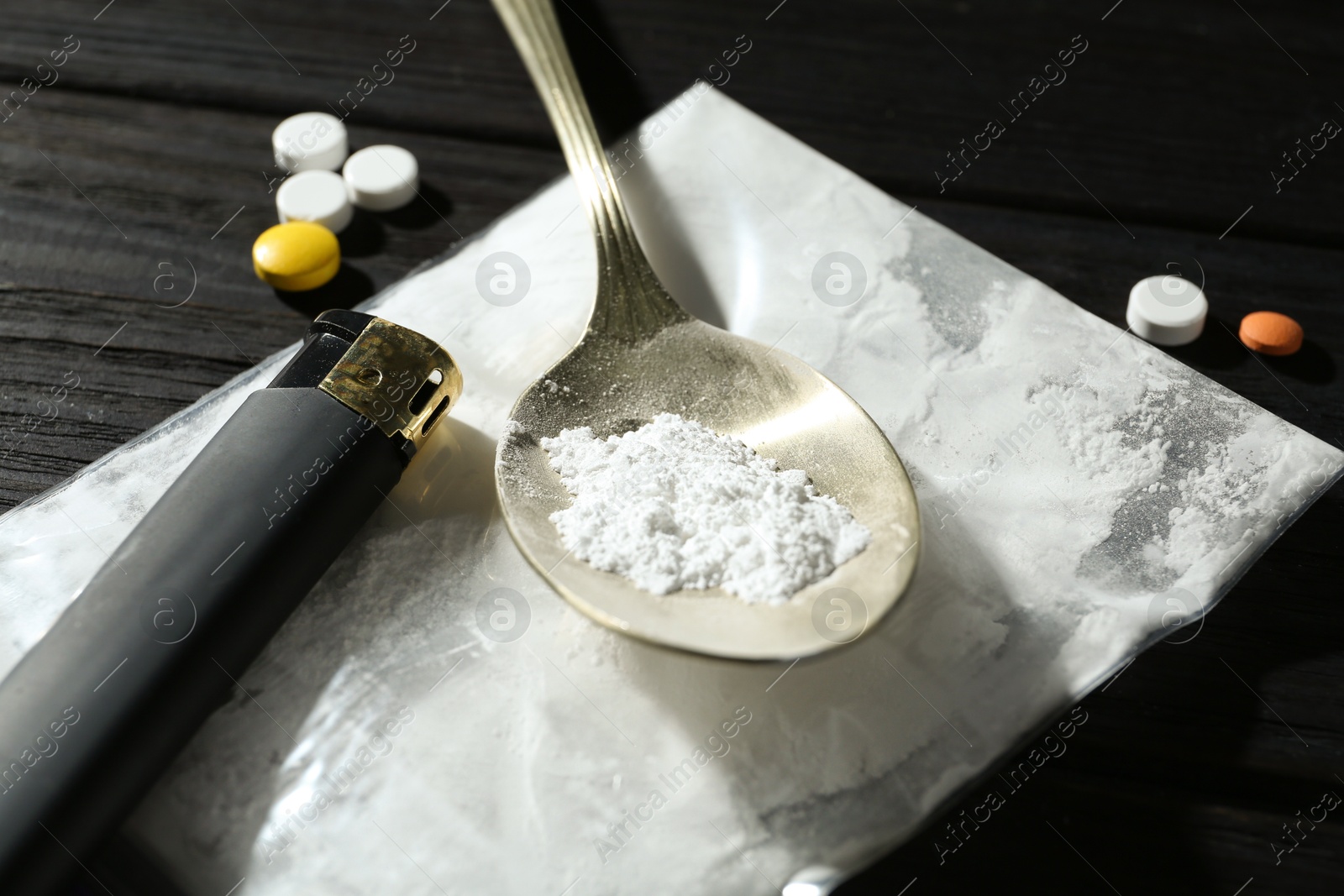 Photo of Drug addiction. Plastic bag with powder, spoon, cigarette lighter and pills on black wooden table, closeup