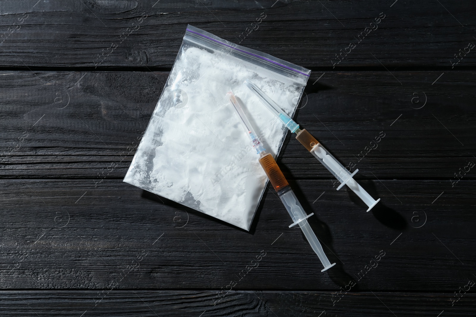 Photo of Drug addiction. Plastic bag with powder and syringes on black wooden table, top view