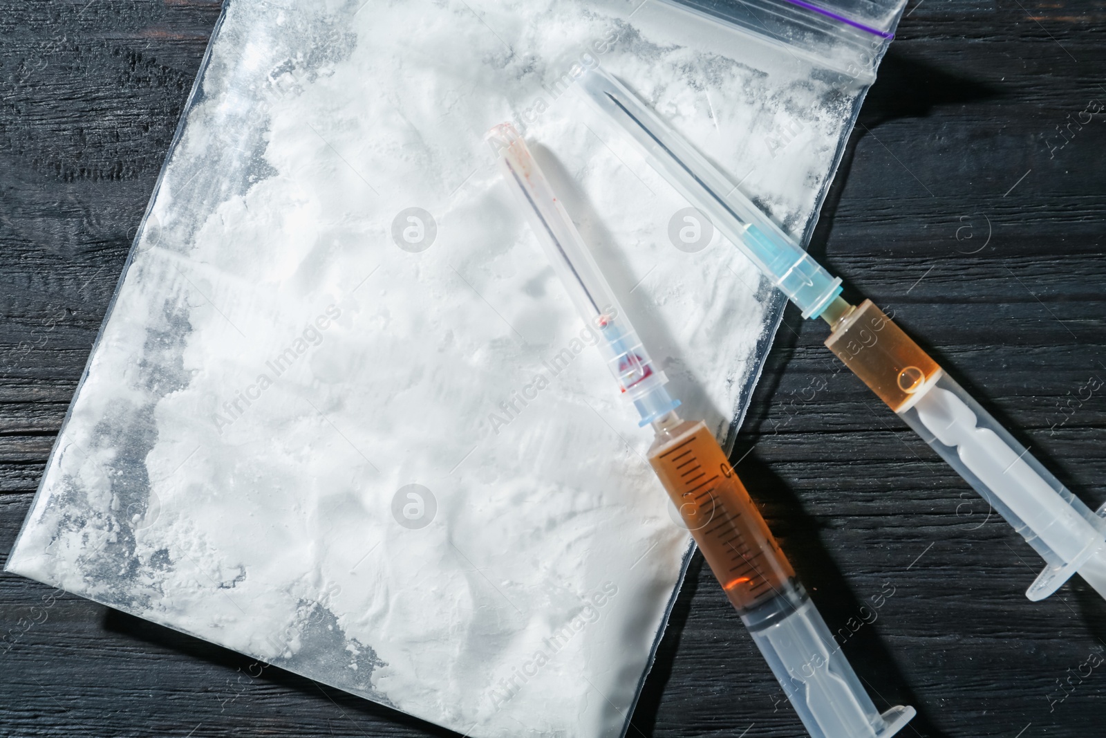 Photo of Drug addiction. Plastic bag with powder and syringes on black wooden table, top view